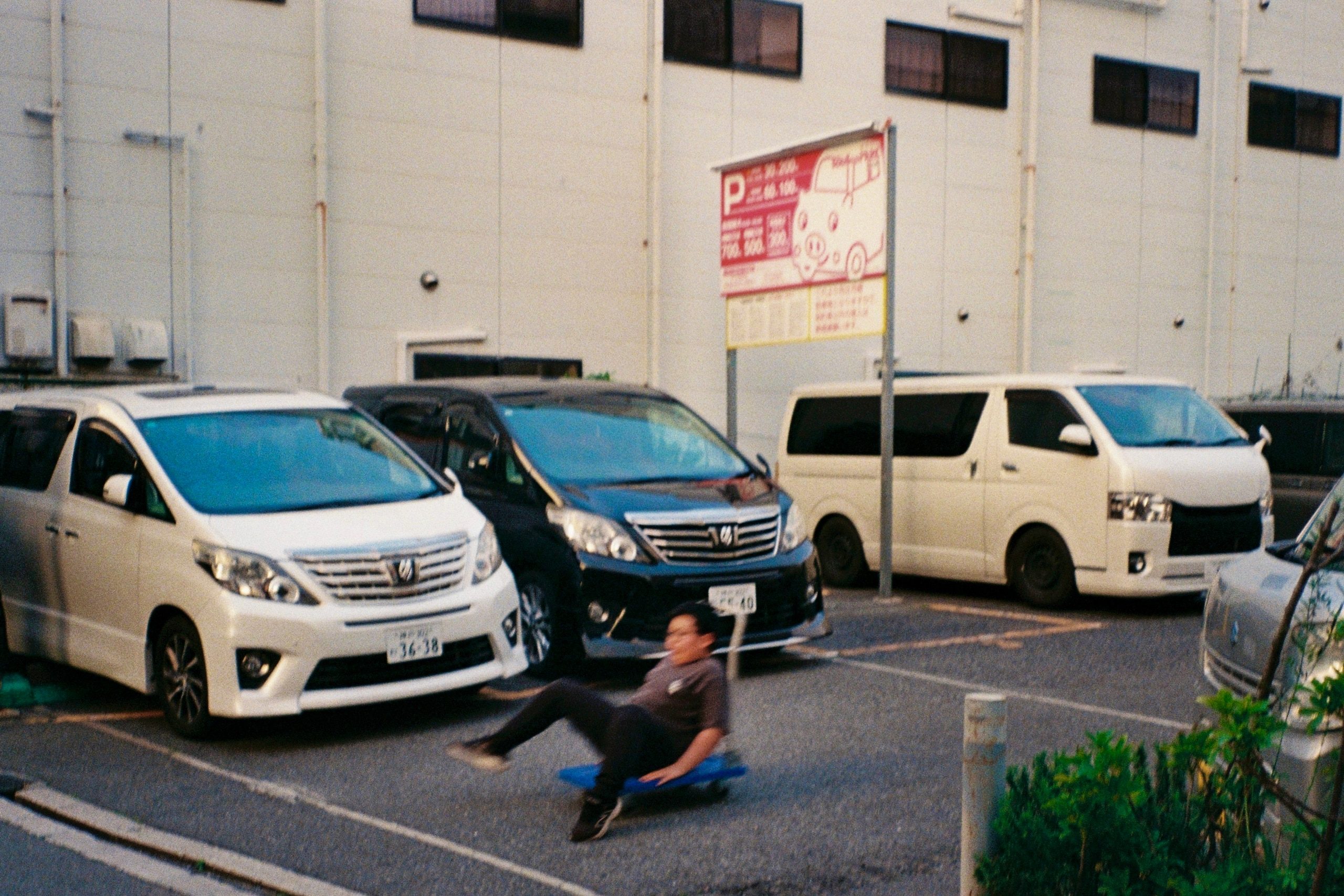 A young person rides low on a skateboard past a row of parked vans.