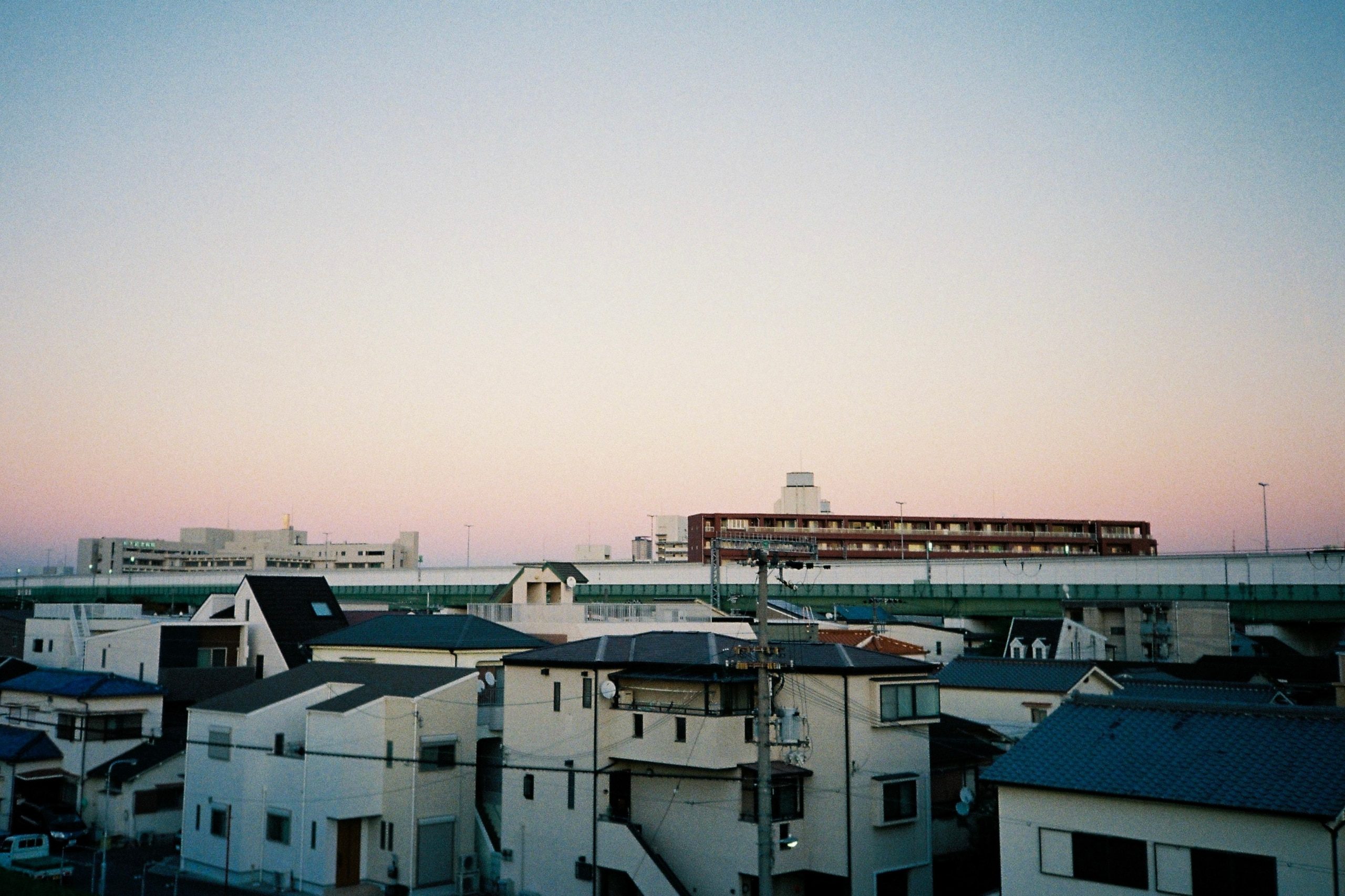 A wide dusk sky fading from blue to pink over a dense suburban rooftop skyline.