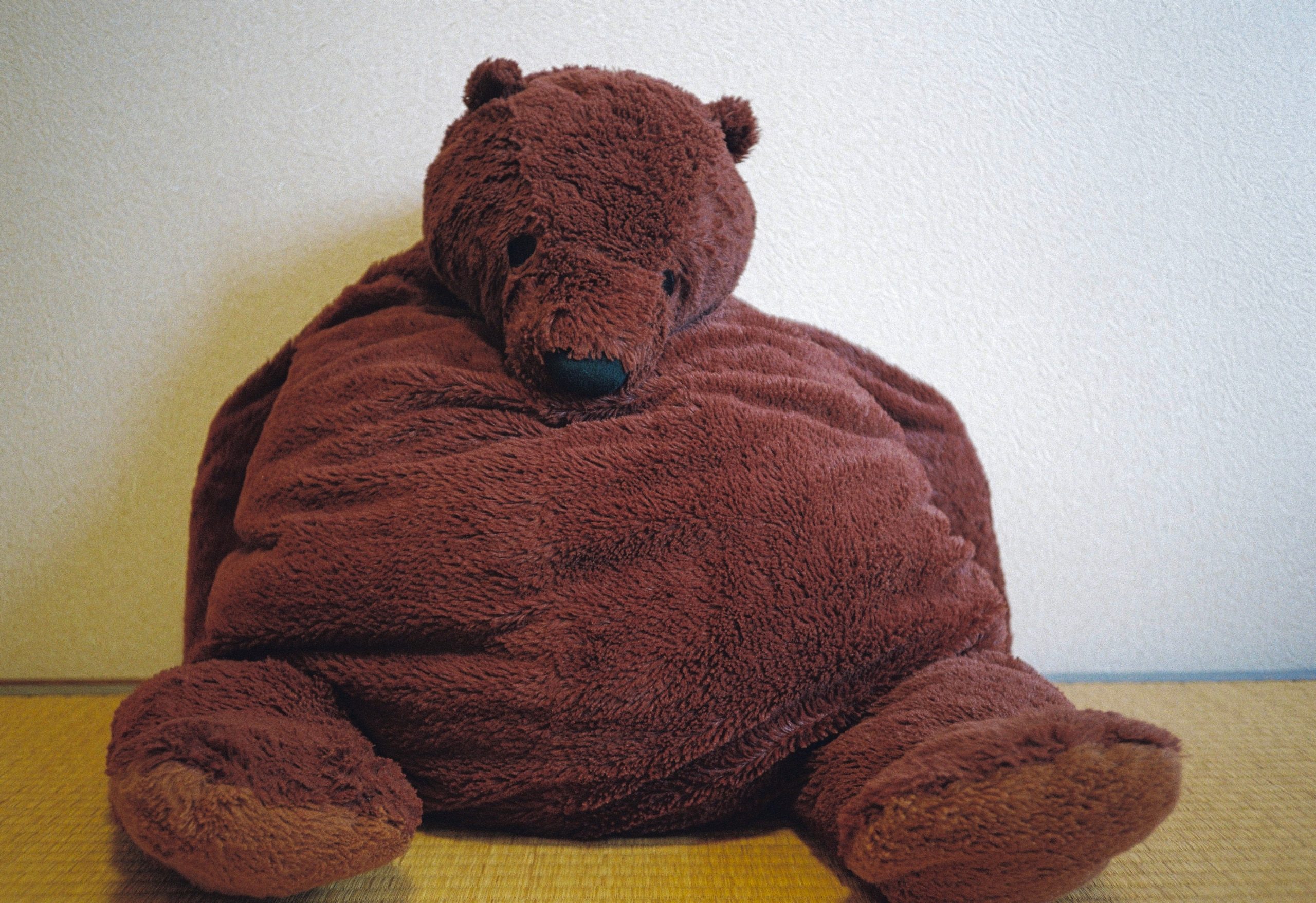 A large, round plush brown bear with a teal nose fills most of the frame, its head resting on its belly.